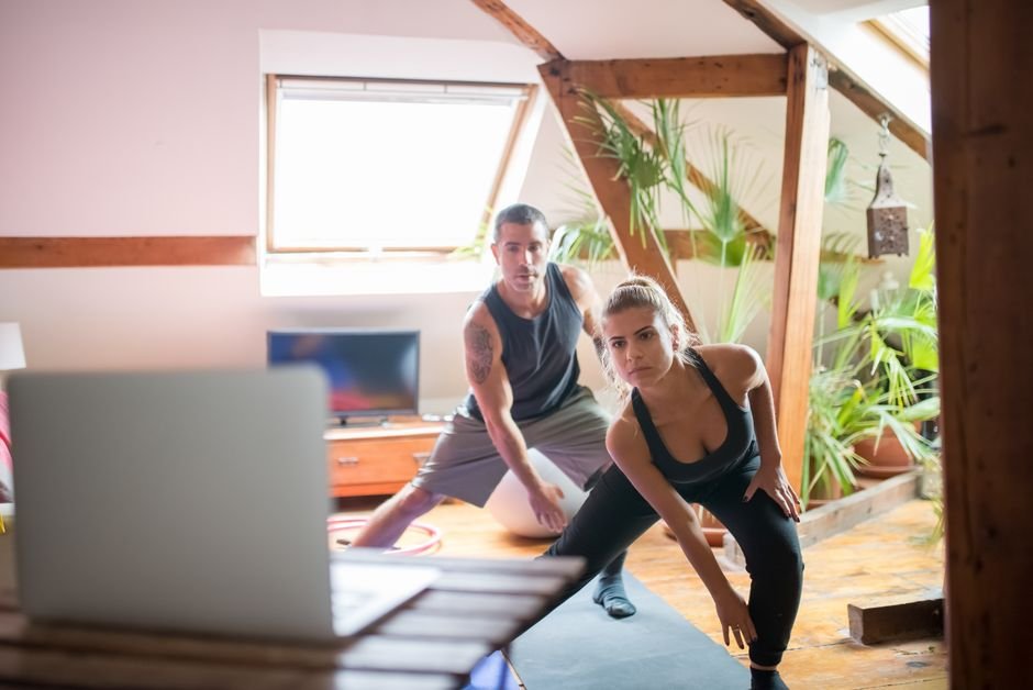 Two people exercising at home with a laptop during an online physical therapy session